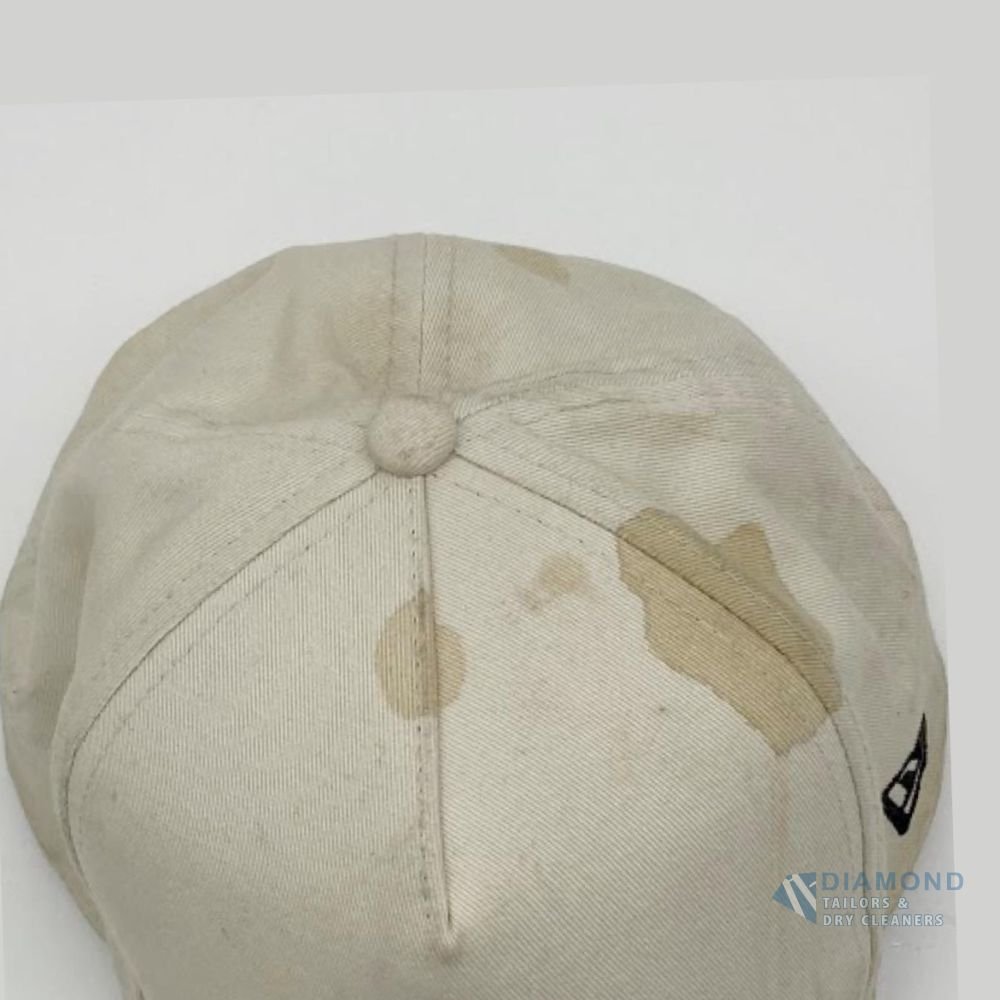 Cream cotton baseball cap before cleaning, with a large brown stain across the crown